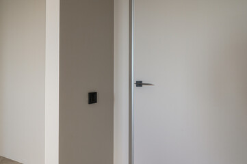 A minimalist interior featuring a closed, white door with a sleek handle. A black electrical outlet...