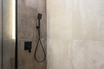 Modern shower detail: black fixture, shower head, and control against tiled walls. Minimalist design with light