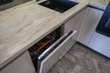 Modern kitchen view. Open dishwasher next to sink with marble countertop