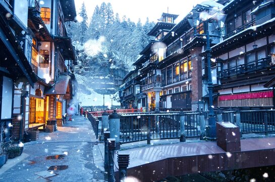 Dawn scenery of Ginzan Onsen after snowfalls, a famous Japanese hot spring town in Obanazawa, Yamagata, Japan, with bridges over a stream flanked by antique wooden buildings on a cold winter morning 