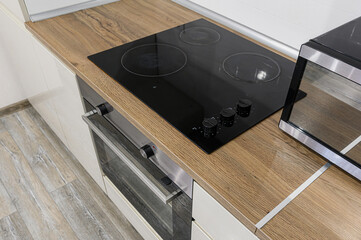 close-up of a kitchen counter with a black electric stove, a built-in oven, and a microwave. The...