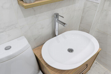 A close-up shows a modern bathroom setup with a white oval sink, chrome faucet, toilet, and tiled walls