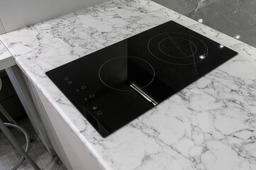 A sleek black induction cooktop sits atop a marble countertop, featuring circular heating zones and touch controls