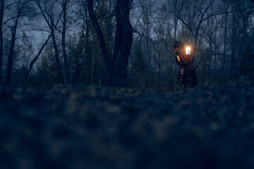 Mysterious figure illuminates dark forest with lantern light.