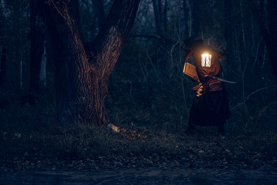 Mysterious figure illuminated by lantern studies ancient tome within shadowy forest.
