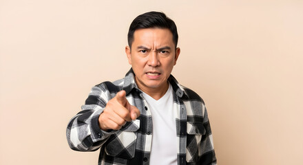 Angry Asian man pointing finger serious expression studio shot beige background mature adult male intense emotion frustrated annoyed discontent disagreement