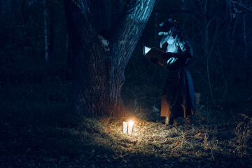 Eerie plague doctor reads illuminated book amidst shadowy forest trees.
