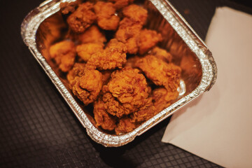 Crispy fried chicken pieces in an aluminum takeout container, shot from above on a dark surface in India.