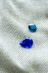 Blue gemstones with brilliant cuts placed on denim fabric background, symbolizing luxury, elegance, creativity, and modern jewelry design inspiration for fashion and accessories.