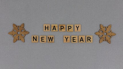 Happy New Year greeting card. Wooden blocks with the text "Happy New Year" and wooden snowflakes isolated on a gray glitter background with copy space.