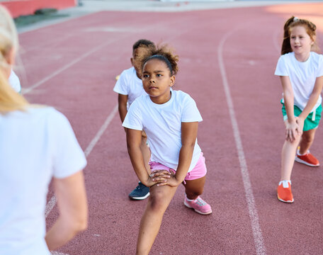 Children exercising and stretching  at the stadium, practice during sports class in school training, little boys and girls in sportswear training as athletes outdoor. Concept of sport, fitness and ach