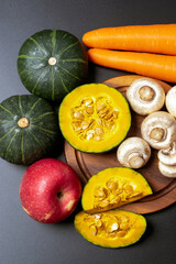 Fresh vegetables and fruits with pumpkin carrot apple and mushrooms on dark background