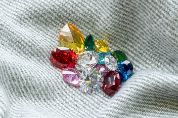 Colorful gemstones in various shapes and cuts placed on denim fabric background, representing...