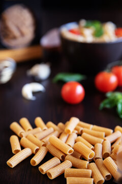 Close-up of Rigatoni pasta on a  table with fresh tomatoes, basil and garlic on a table in the background