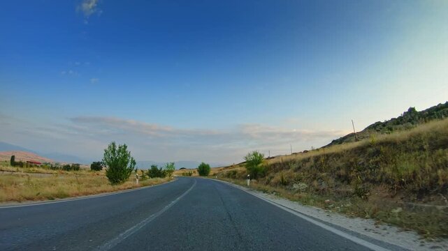POV Car driving across countryside, dry grass, blue sky, summer
