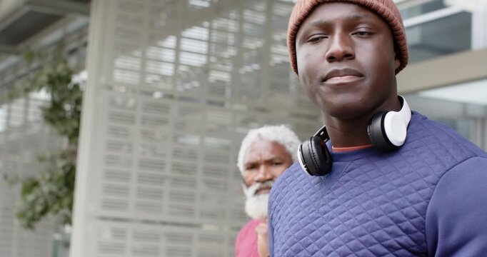 African American father and son exchanging looks after gaze shift while wearing headphones on plaza