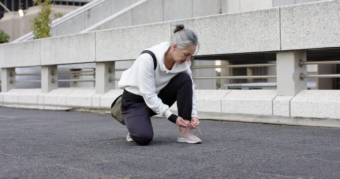 Arriving at terrace, woman kneeling tying sneakers, smiling at passing exerciser with yoga mat