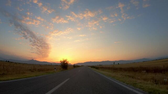 POV vehicle driving on cracked asphalt road at sunset, golden fields
