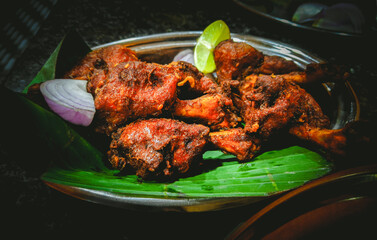 Spicy fried chicken dish, served on a banana leaf in a metallic plate, close-up composition, Karnataka, India.