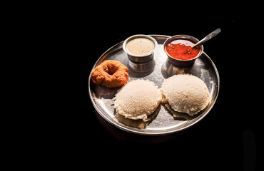 Delicious South Indian breakfast: idli, vada, sambar, and chutney served on a metal plate against a dark background.  Karnataka, India.