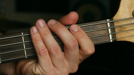 Close up musician fingers moving along fretboard of bass guitar, pressing strings to play different notes, chords during musical performance or practice session. Musician playing on bass guitar