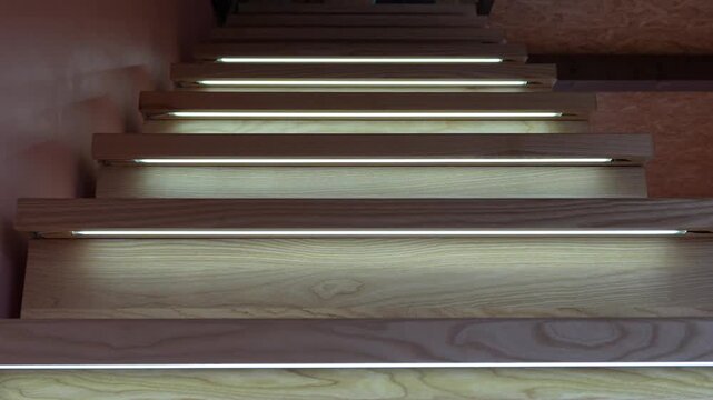 Modern wooden staircase with LED step lighting turning on, interior design concept