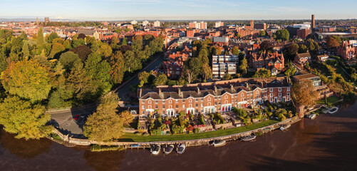 Aerial view of Chester’s riverside with Georgian houses, moored boats, and lush greenery under morning sunlight.