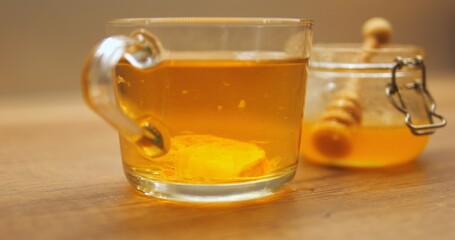 Slice of lemon sinks to bottom in tea cup contributing to sour flavor of drink. Beverage with citrus against honey jar maintains hydration and essential nutrients