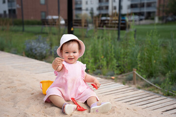 delightful toddler in pink dress happily plays in sandy park, showcasing innocence and joy amidst...
