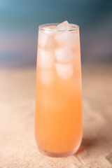 chilled refreshing peach-colored beverage in tall glass with ice cubes on warm soft focus background evoking a summery and inviting atmosphere, bubbly, ocean, sea, backdrop, sandy, blissful, leisure