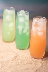 three colorful iced drinks in tall glasses on sandy surface with a blurred gradient background evoking a refreshing beachside feel with vibrant hues and a relaxed vibe, calm, soft, relaxation