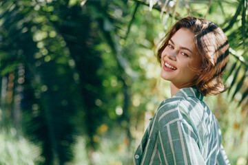 Portrait of a cheerful woman outdoors in sunlight, wearing a striped shirt, smiling over her...