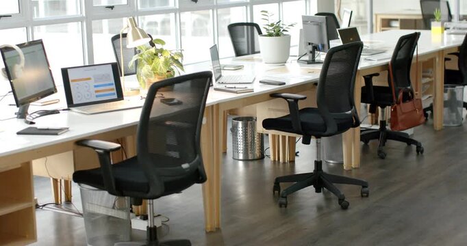 Camera holding steady shot of empty workstation under windows, showcasing monitor, laptop, tablet