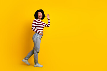 Fototapeta premium Cheerful young woman with curly hair in casual style waving on yellow background