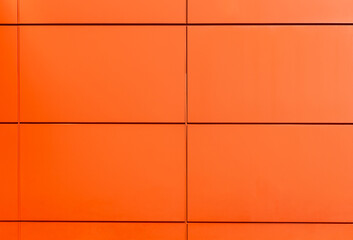 Orange wall with rectangular metal panels creating modern geometric pattern. Minimalist architectural background with clean lines and vibrant colour, ideal for design, construction, abstract concepts