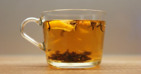 Tea leaves and fresh lemon slice rotate in transparent mug with hot water. Process of brewing herbal beverage in glass cup on wooden table