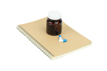 Amber glass medicine bottle with blue and white capsule pills on a notebook, isolated on white background with clipping path.