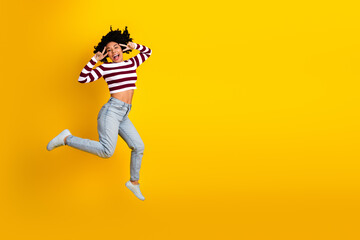 Energetic young woman jumping joyfully against a vibrant yellow background, expressing happiness