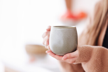 Person holding ceramic cup with blurred background, cozy ambiance, minimalist home decor, warm beverage