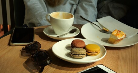 Woman delights in comfort of cup of coffee and sweetness of macarons and pastry. Smartphone and fashionable sunglasses add modern touch to moment