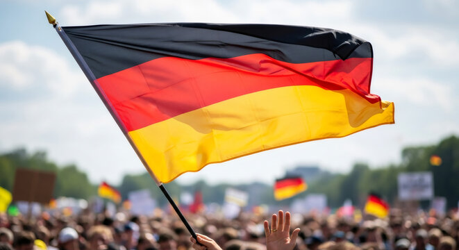 Woman hand holding german flag at crowd protest outdoor. National symbol waving in wind. Human rights day.