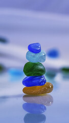 A meticulously arranged stack of vibrant, translucent glass beads in shades of sapphire blue, emerald green, and sunlit yellow takes center stage. The beads, with their intricate internal patterns and