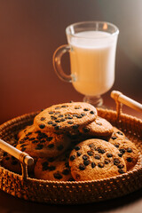 Freshly baked chocolate chip cookies and a glass of milk on a wooden table