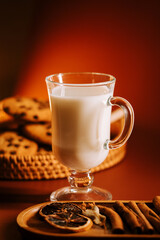 Warm milk beside cookies and dried fruit slices on a cozy orange background
