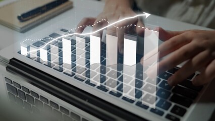 A close-up view of hands typing on a laptop keyboard with digital growth graphs displayed, representing business analysis, financial trends, and modern workspace efficiency. Copula