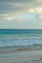 Calm ocean waves under cloudy sky at sunrise. Peaceful seascape with blue water and warm morning light on the horizon.
