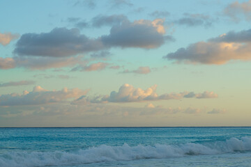 Calm ocean waves under pastel sunset sky with soft clouds. Peaceful seascape view of turquoise sea and golden light on the horizon, nature background.
