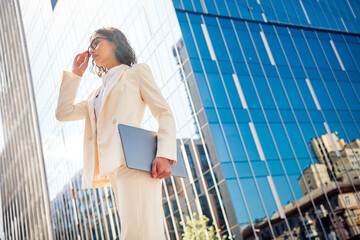 Fototapeta premium Young professional businesswoman in elegant attire outdoors against a modern office building, radiating confidence and ambition