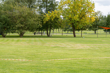 Lawn with Red-White Tape. A large green lawn with red-white marking tape laid out. Trees and fences form the background of this organized outdoor space.