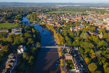 Aerial view of Chester suspension bridge crossing the River Dee, with boats and cityscape beyond.